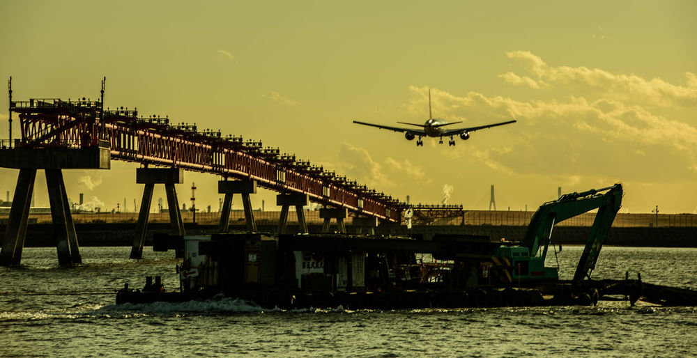 Low angle view of airplane flying over sea against sky during sunset
