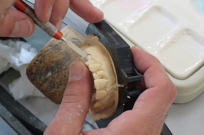 Cropped hands of male dentist making dentures mold at desk