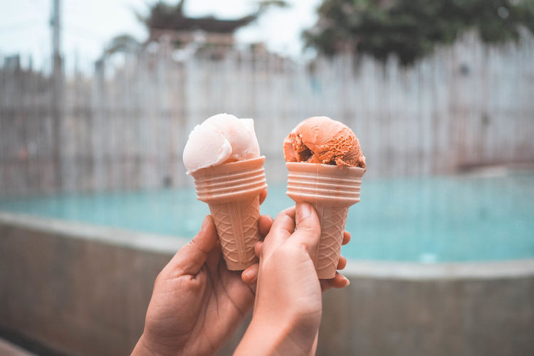 Cropped hands holding ice cream cone against fountain
