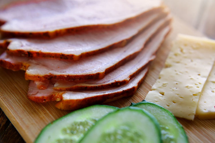 Slicing ham, cucumbers and cheese with ruddy thin breads lie on a wooden board.