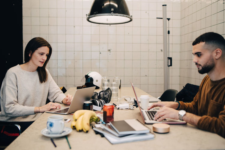 Young male and female hackers using laptops for coding at desk in small office