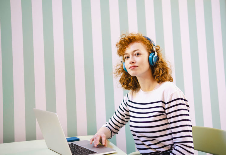 Young woman with laptop listening music through headphones in cafe