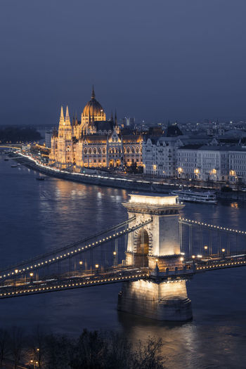 Illuminated bridge over river in city at night