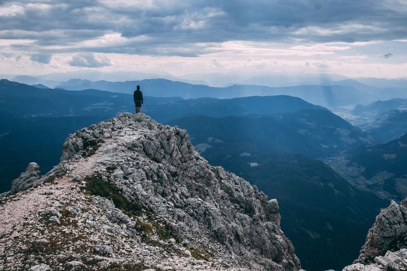 Rear view of man looking at landscape while standing on mountain against cloudy sky