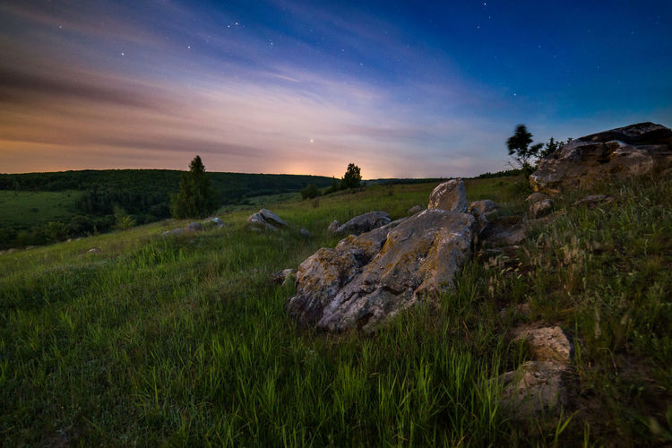 Scenic view of land against starry sky during sunset