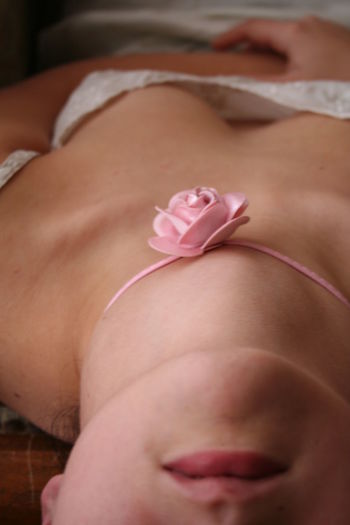 Midsection of woman lying on bed with artificial pink rose tied on her neck