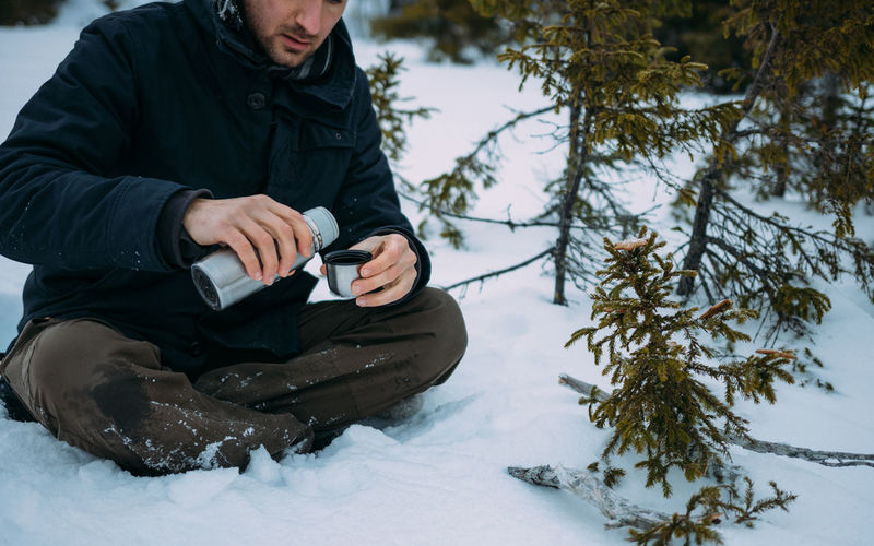 Man holding insulated drink container while sitting on snow covered field