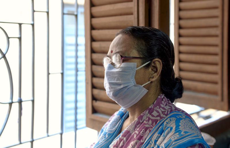 An aged bengali woman wearing surgical face mask, casually looking out of window