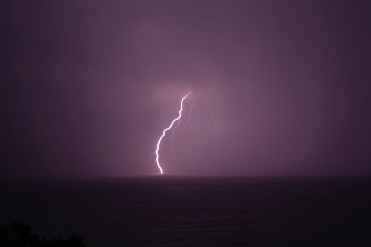 Scenic view of sea with lightning in sky at night