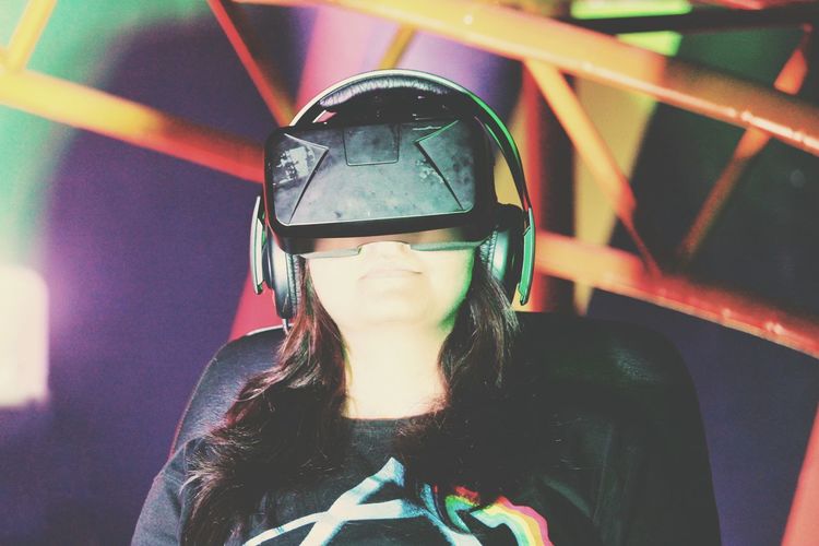 Close-up of woman wearing virtual reality simulator while sitting on chair against wall