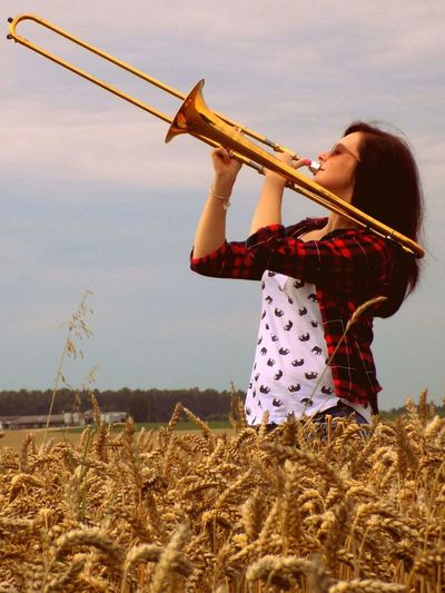 Side view of young woman playing trumpet on field against sky