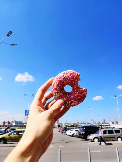 Cropped hand of person holding donut against sky