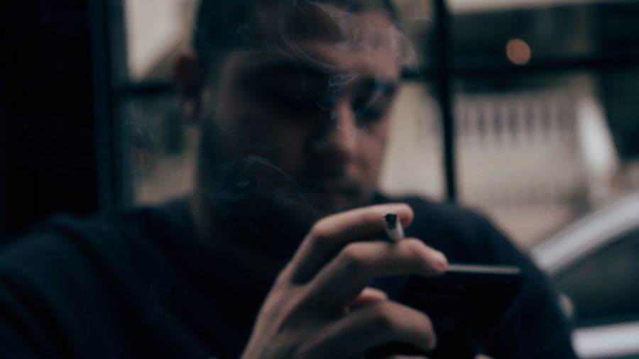 Close-up of man holding cigarette using smart phone