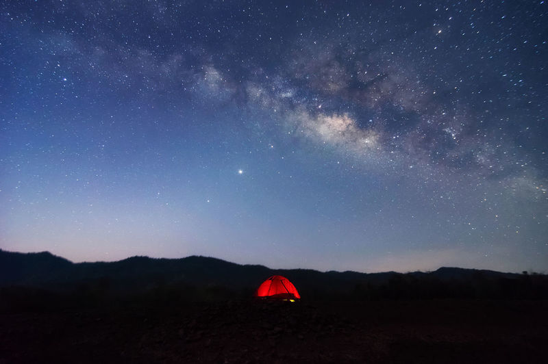 Red tent in reservoir under milky way galaxy with stars space dust in the universe, long exposure. 