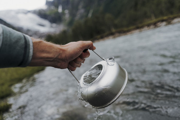Cropped hand holding water in tea kettle