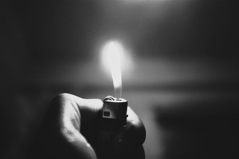 Close-up of hand holding cigarette lighter with flame at night