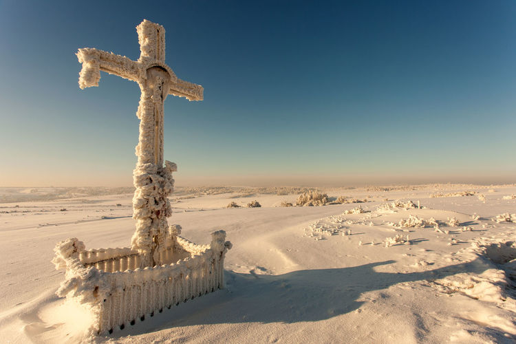Cross on snow covered land against clear sky