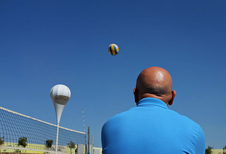 Low angle view of bald man and ball against clear sky on sunny day