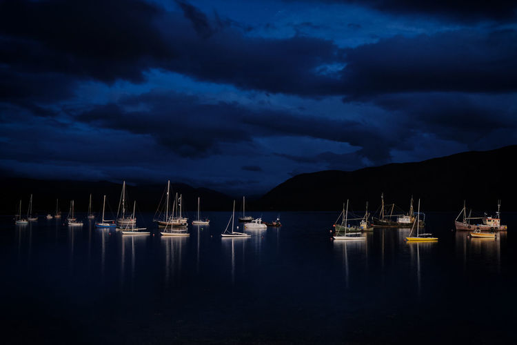 Sailboats moored in sea against sky at night