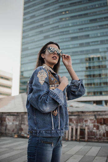 Young woman wearing sunglasses while standing against building in city