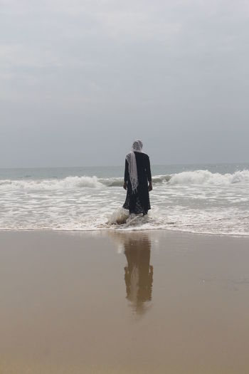 REAR VIEW OF MAN ON BEACH AGAINST SKY