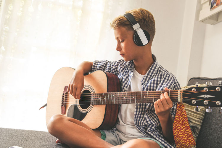 Boy playing guitar while sitting on sofa at home