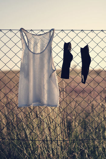 Tank top and socks hanging on chainlink fence against sky
