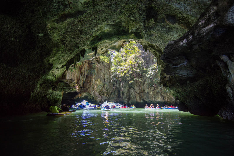Group of people rowing boats in river by cave
