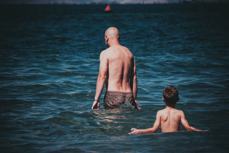 Rear view of shirtless man with son in sea
