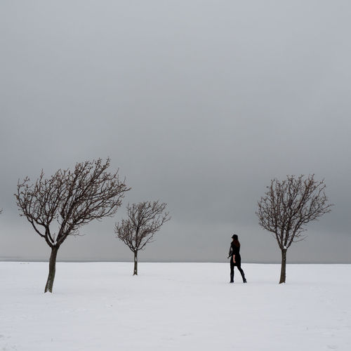 Woman standing on snow covered field by bare trees