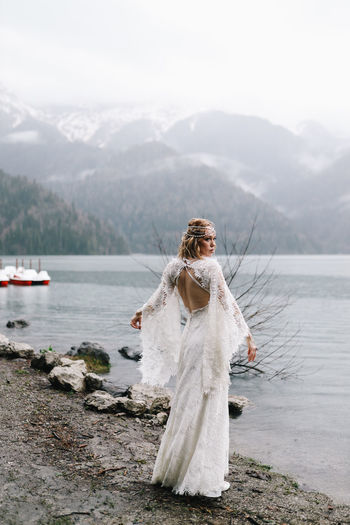 A tender sensual young woman bride in a fashionable wedding dress is standing in the rain in nature