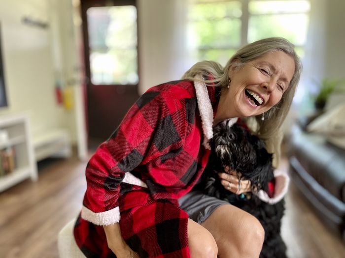 Active senior woman smiling hugging pet dog and wearing red and black plaid holiday robe.  