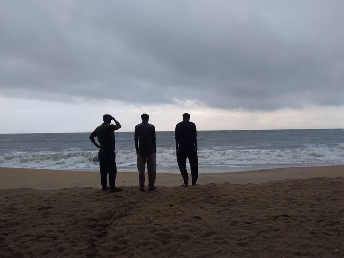 Friends standing on beach against sky