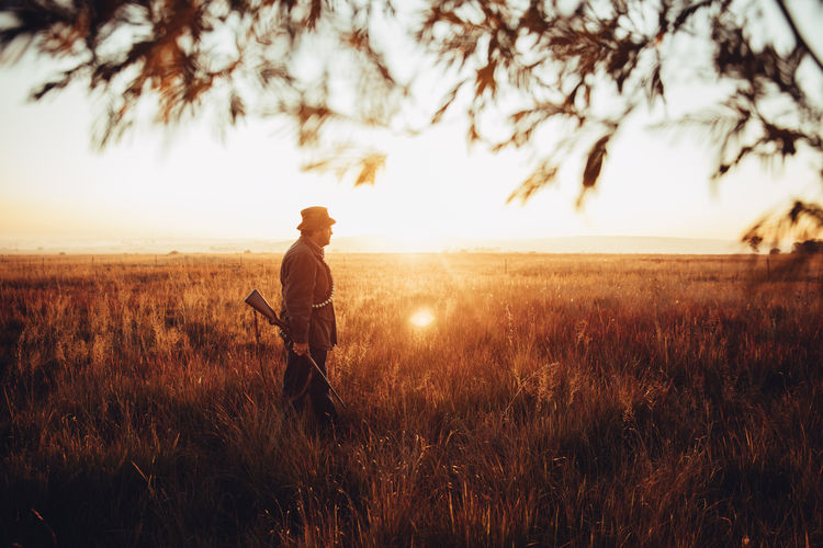 Hunter with shotgun standing in field during sunrise