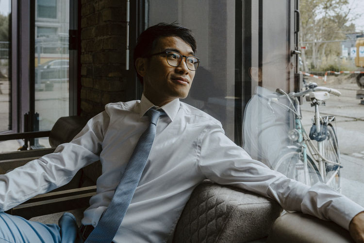 Male entrepreneur looking through window while sitting on sofa at office