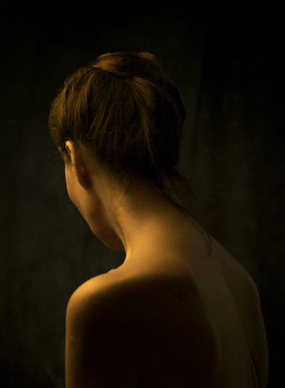 Close-up of young woman looking away against black background