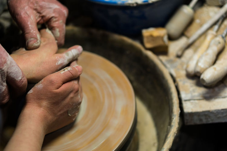 Cropped hands of worker teaching person pottery in workshop
