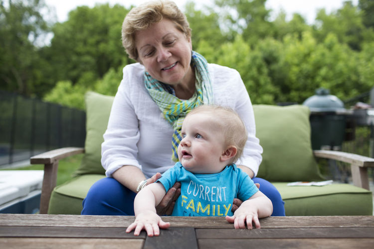 Happy grandma sits on outdoor sofa holding baby grandson