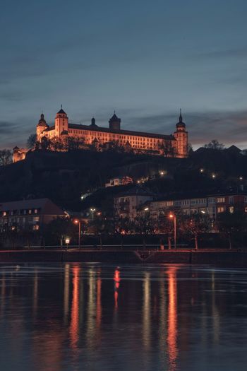 Castle and buildings by river against sky at night