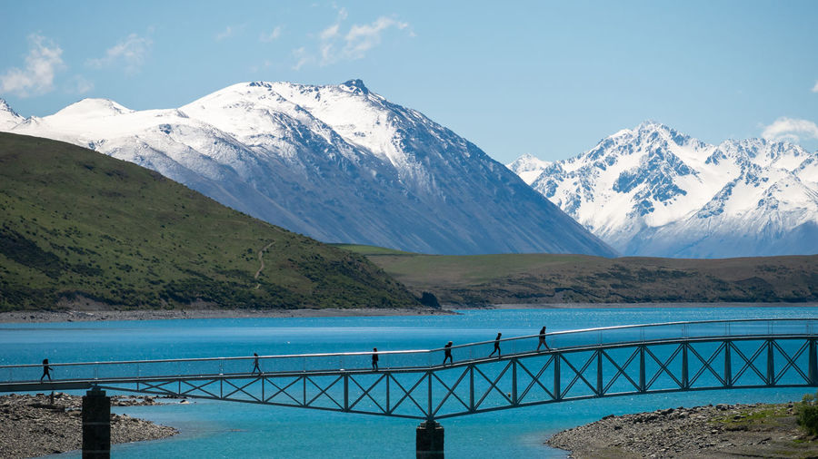 People on the bridge above turquoise lake with snowy mountains in backdrop.lake tekapo, new zealand