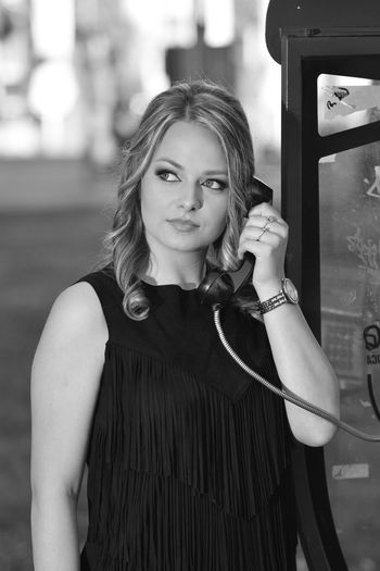 Portrait of young woman standing outdoors by the telephone booth