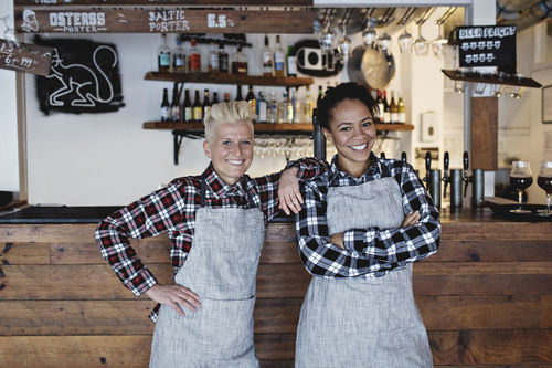 Portrait of smiling female bartenders standing against bar counter