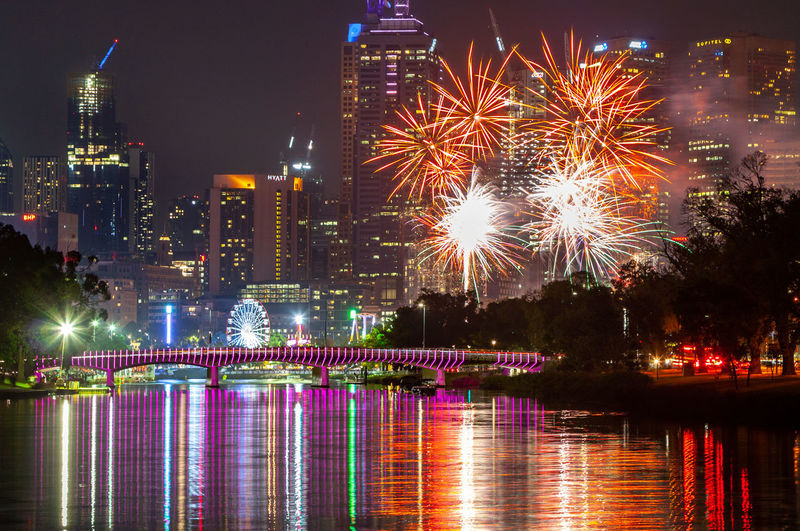 Firework display over illuminated buildings in melbourne city reflected in the yarra river at night