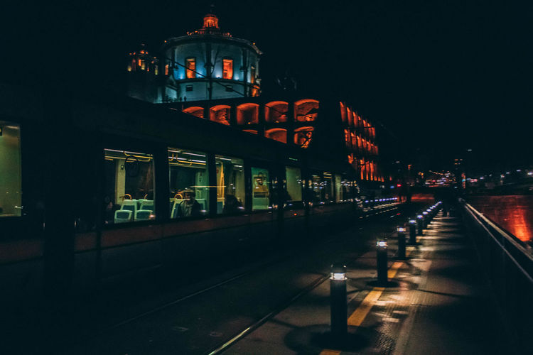 Illuminated railroad station by buildings in city at night