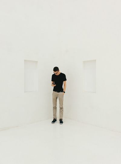 Man using phone while standing in corner of white room