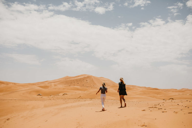 Rear view of men walking on desert against sky