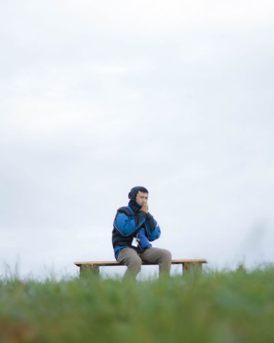 Full length of man sitting on field against sky