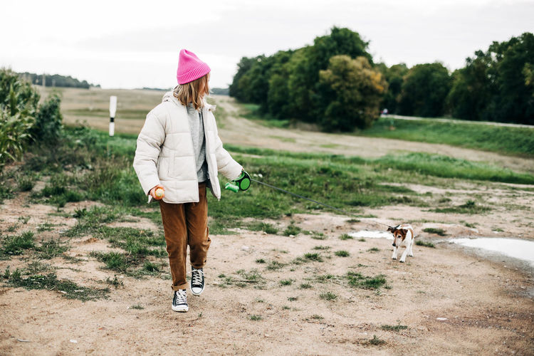 Cute teenage girl walking her dog jack russell terrier on a leash in a field against a background 