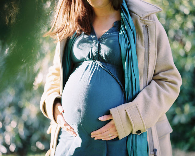 Midsection of pregnant woman standing against trees