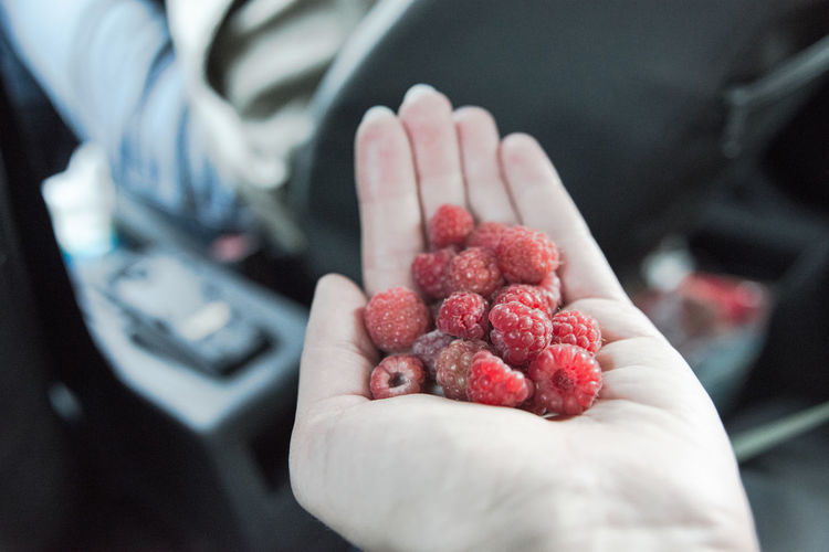 Cropped image of hand holding raspberries in car